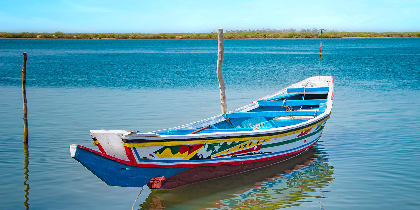 Traditional colorful wooden boat on the river in sea lagoon and a beautiful sky in the background, Africa, Senegal.