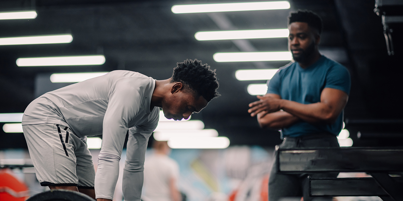 Determined young athlete lifting weights with personal trainer i