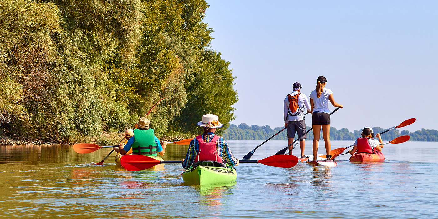 Group of friends (people) travel by kayaks. Kayaking in wilderness of Danube river in summer. Peacefull nature scene of calm river. Water tourism concept.