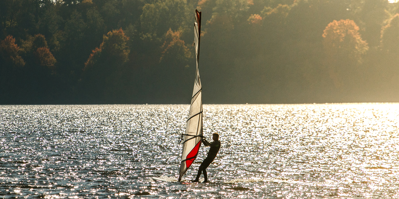Windusrfer in the sunset. Man windsurfing with on board in beaut
